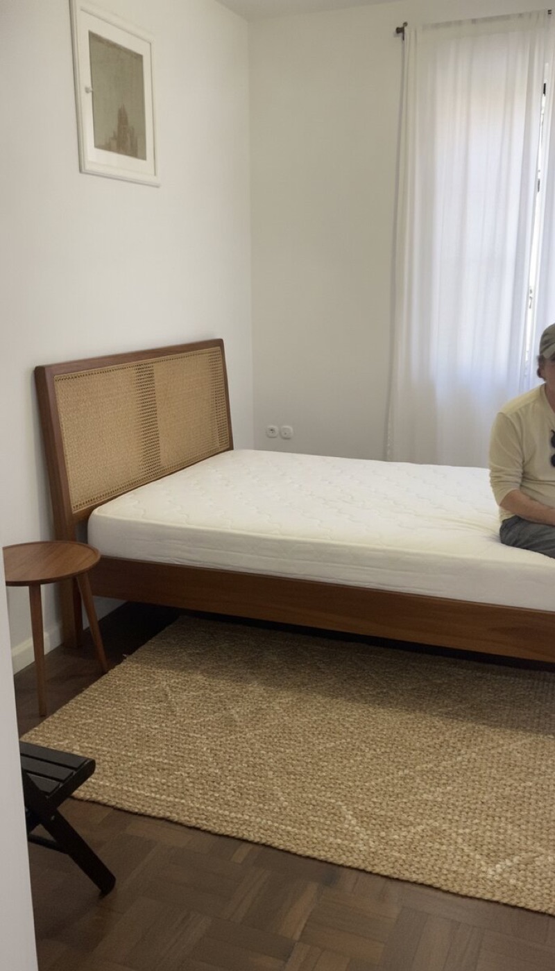 Same room with a solid wood bed frame, cane headboard, rug and side table