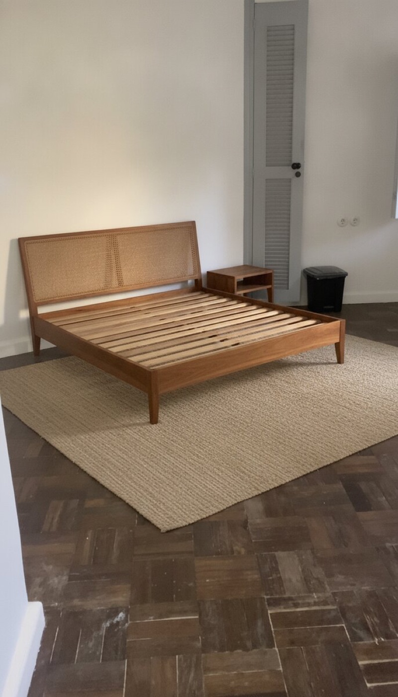 Same room with a solid wood bed frame, cane headboard, rug and side table