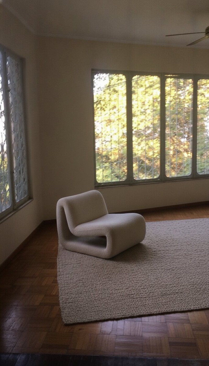 Same room repainted warm cream with a sculptural chair and rug added