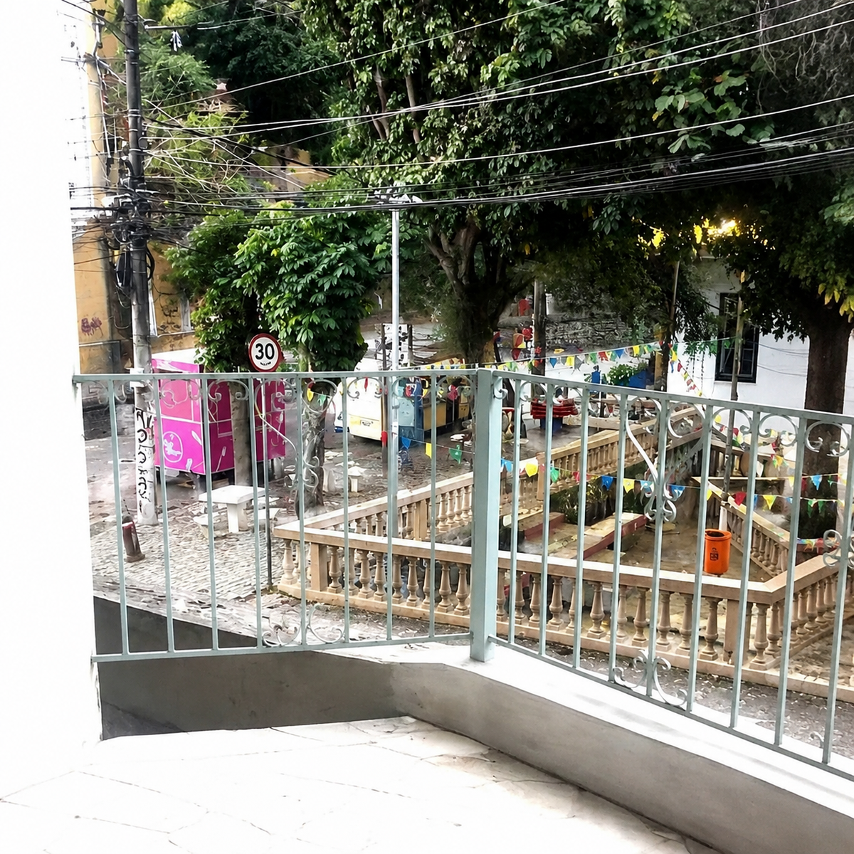 Empty balcony with railing overlooking a bunting-strung Santa Teresa street corner, no furniture