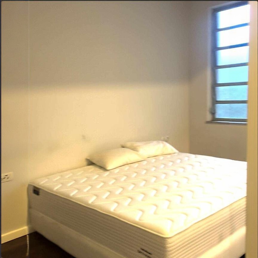 Bedroom with bare mattress and barred window, no bedding or other furniture