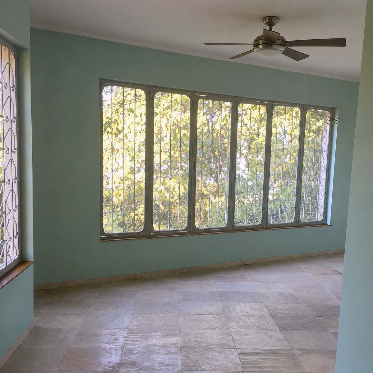 Empty room with sage green walls, marble floor, garden-view windows, and a ceiling fan, no bed
